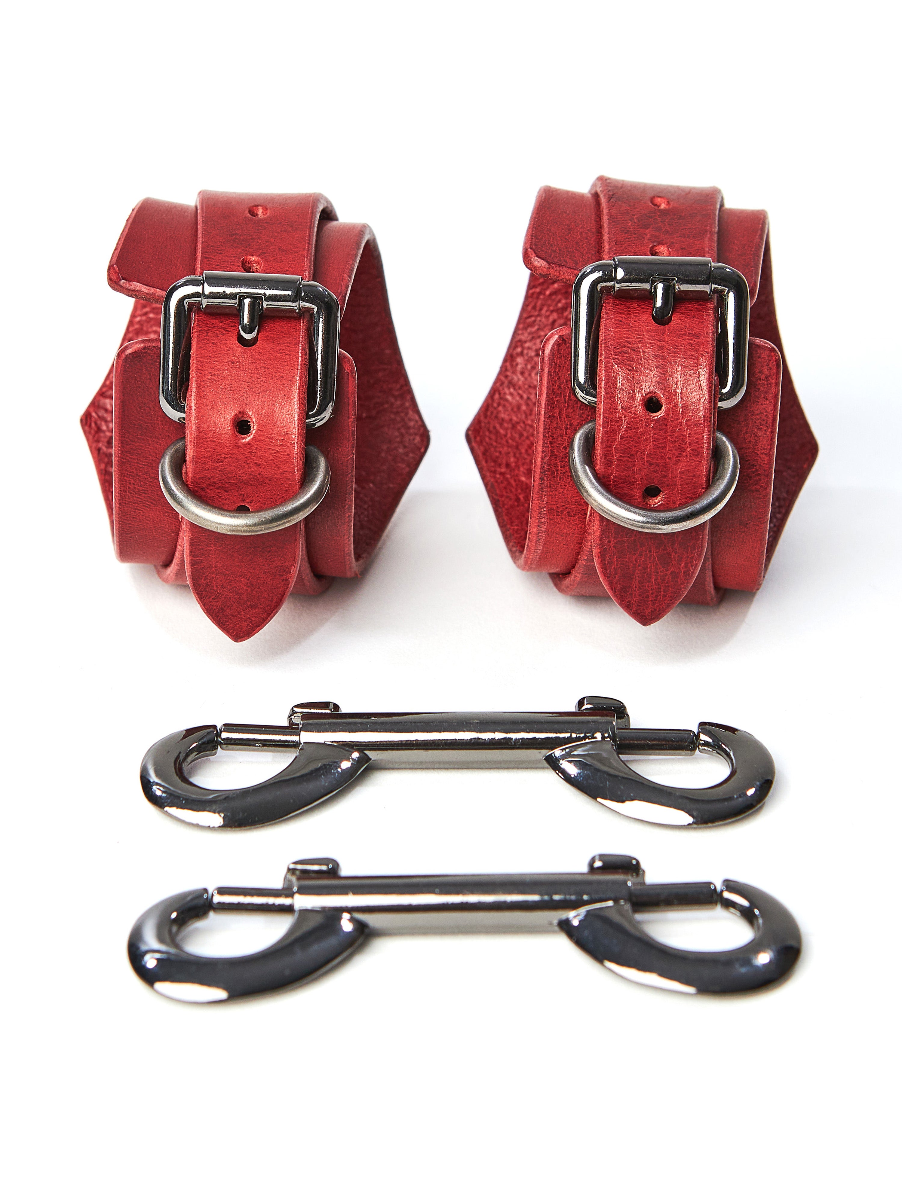 Close-up of handcuffs, with two double carabiners lying side by side. Handcuffs in the form of a rhombus. Leather 2.4-3 mm thick with dark nickel-colored hardware. Red leather.