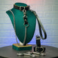Leather collar with chain leash and handcuffs on a green mannequin bust against a textured wall.