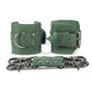 Green leather handcuffs with two connectors with carabiners are lying side by side, one handcuff is shown with a buckle and it stands on a rib, the second handcuff is shown with a D-ring for which the carabiners are attached and it also stands on a rib. Front view. Dark nickel hardware. 