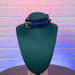 Blue leather choker on a green mannequin bust against a textured purple and blue background