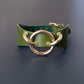 Green leather choker with gold metal rings on a dark background