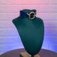 Blue leather  with gold ring on a mannequin bust against a textured purple wall.ollar