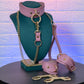 Pink leather choker, leash, and handcuffs on a mannequin bust against a textured wall.