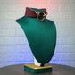 Green velvet mannequin bust with a marsala leather collar and gold ring on a textured white background