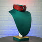 Red leather collar on a green mannequin bust against a textured white wall.