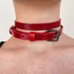 Red leather choker with a silver buckle worn around the neck on a plain background