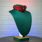 Red leather collar on a green mannequin against a textured white wall.