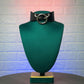 Black leather choker with silver ring on a green mannequin bust against a textured white brick wall.