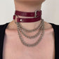 Person wearing a burgundy leather choker with metal chain necklaces on a plain background