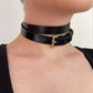 Black leather choker with a gold buckle worn by a person on a plain background