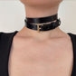 Black leather choker with a gold buckle worn by a person on a plain background