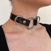 Black leather choker with metal rings worn by a person on a plain background