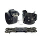 Black leather handcuffs with two connectors and carabiners lie side by side, one handcuff is shown from the side of the buckle and lies half sideways the second handcuff stands half sideways and is shown from the side of the D-ring for which the carabiner is fixed. Dark nickel hardware. 