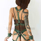 Wide chest harness with bondage garters with handcuffs attached to the garters with D-rings. Rooney handcuffed to the gaiters by the ring. Rear view. Green leather. Gold-tone hardware.