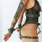 Wide chest harness with bondage garters with handcuffs attached to the garters by D-rings. Rooney handcuffed to each other. Side view. Green leather. Gold colored hardware.