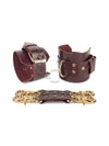 Marsala leather handcuffs with two connectors and carabiners lie side by side, one handcuff is shown from the side of the buckle and lies half sideways the second handcuff stands half sideways and is shown from the side of the D-ring for which the carabiner is fixed. Gold hardware. 