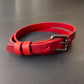 Red leather choker with a dark nickel buckle on a gray background