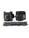 Black leather handcuffs with two connectors with carabiners are lying side by side, one handcuff is shown with a buckle and it stands on a rib, the second handcuff is shown with a D-ring for which the carabiners are attached and it also stands on a rib. Front view. Dark nickel hardware. 