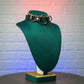 Black leather collar on a green mannequin bust against a textured white brick wall.