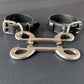 Two black leather handcuffs with silver metal clasps on a dark surface
