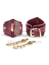 The handcuffs are diamond shaped, one handcuff is shown on the side of the D-ring to which the carabiners are attached, the other on the buckle side. There are two double carabiners next to it.
Dark crimson colored leather, gold hardware. Front view.