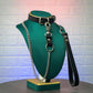 Black leather collar with chain leash on a green mannequin bust against a textured white wall.