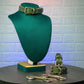 Green leather bondage collar on a mannequin bust with handcuffs on a table against a textured wall.