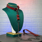 Red leather collar with chain leash on a green mannequin against a textured white wall.