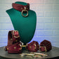 Set of leather collar and handcuffs with ankle cuffs on a green mannequin bust against a textured white wall.