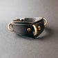 Black leather collar with gold hardware on a gray background