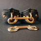 Black leather handcuffs with gold hardware on a dark gray background