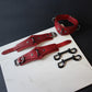 Red leather collars and cuffs on a white surface with a dark background