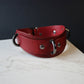 Red leather collar with black hardware on a marble surface with a dark background
