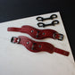 Two red leather handcuffs with metal buckles on a marble surface.