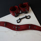 Red leather collar and cuffs with metal hardware on a white marble surface.