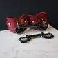 Red leather handcuffs with black hardware on a marble surface