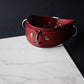 Red leather collar with silver hardware on a marble surface with a black background