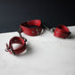 Red leather handcuffs on a white surface with a dark background