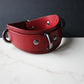 Red leather collar with metal hardware on a white surface and dark background