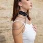 Woman wearing a black leather choker necklaces against a beige stone wall.