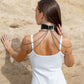 Woman wearing a black leather choker necklaces against a beige stone wall. Back view