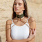 Woman wearing a green leather choker necklaces against a beige stone wall.