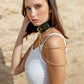 Woman wearing a green leather choker necklaces against a beige stone wall.