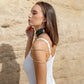Woman wearing a green leather choker necklaces against a beige stone wall.