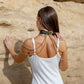 Woman wearing a green leather choker necklaces against a beige stone wall.
