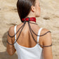 Woman wearing a red leather choker necklaces against a beige stone wall. Back view